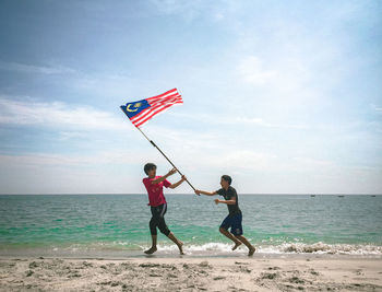 Men running with flag on beach against sky