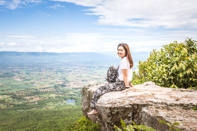 Young woman sitting on rock against sky
