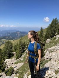 Woman seing on rock by mountains against sky