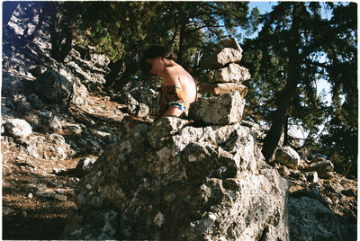 Full length of shirtless man on rock against trees