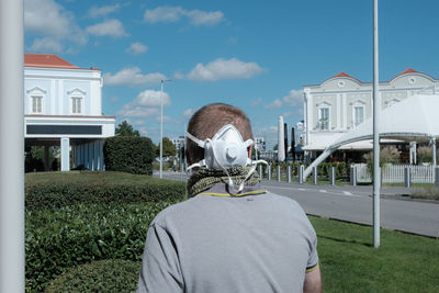 Rear view of person with mas on the neck against built structure against sky