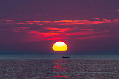 The golden sun rising beyond lighthouse and fisherman in the ocean.