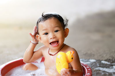 Cheerful shirtless baby girl sitting in bathtub