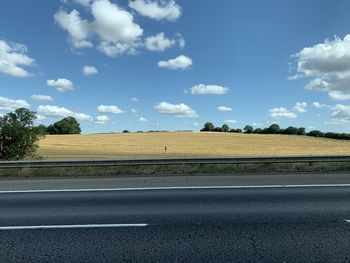 Empty road amidst field against sky