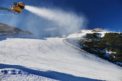 Skier near a snow cannon making fresch snow. mountain ski resort and winter calm mountain landscape.