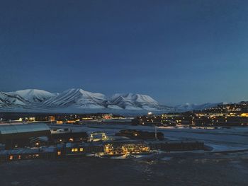 Illuminated city and snowcapped mountains against clear sky at night