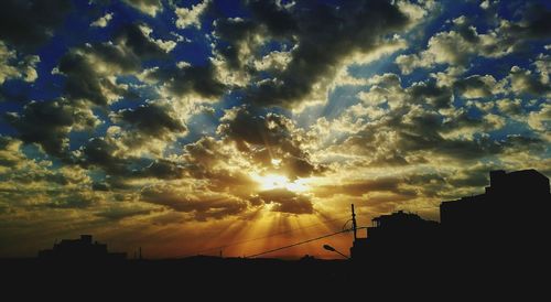 Silhouette buildings against cloudy sky at sunset