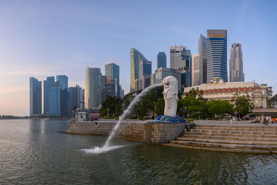 Modern buildings by river against sky in city