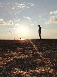 Man standing on beach against sky at sunset