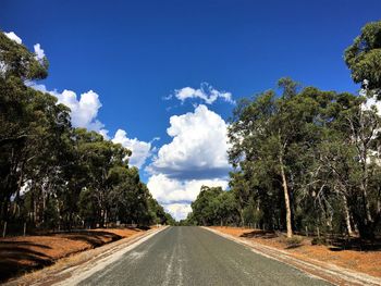 Road amidst trees against cloudy sky