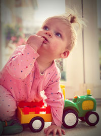 Cute baby girl looking away while sitting by toys on floor at home