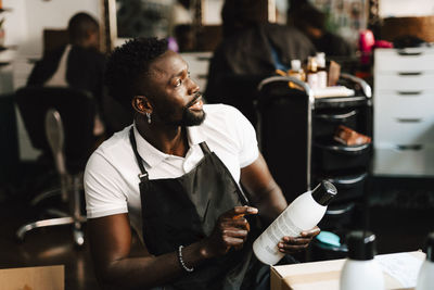 Male barber with beauty product looking away in hair salon