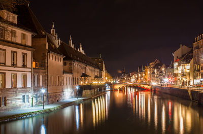 Bridge over river by illuminated buildings in city at night