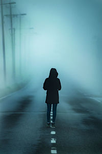 Rear view of woman standing on road during foggy weather at night