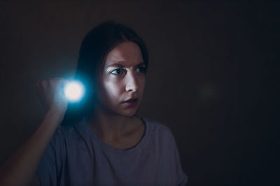 Portrait of young woman standing against black background