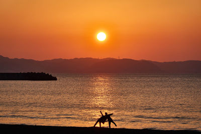 Silhouette people on beach against orange sky