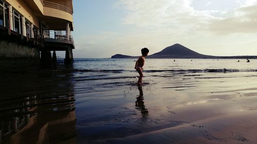 Boy standing on shore against sea during sunset