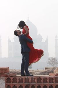 Side view of woman holding red umbrella against sky in city