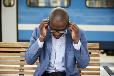 Businessman adjusting in-ear headphones while sitting at railroad station