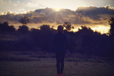 Rear view of man walking on field during sunset