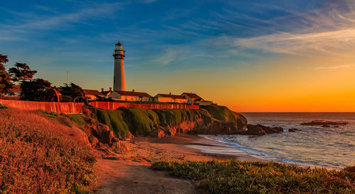 Lighthouse by sea against sky during sunset