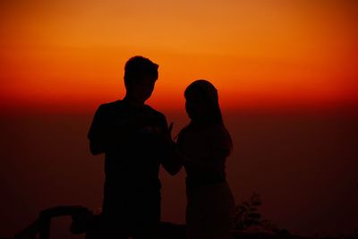 Silhouette couple standing against orange sky during sunset