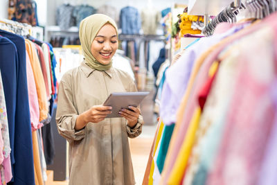 Smiling woman in hijab using digital tablet in clothing store