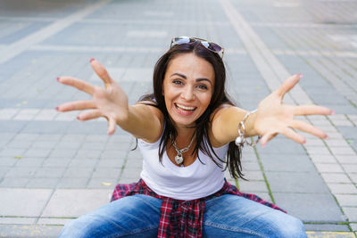 Happy girl in white t-shirt, blue jeans and white sneakers sits on sidewalk