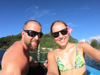 Portrait of smiling man and woman wearing sunglasses in boat in sea against sky