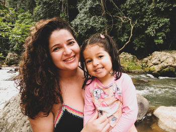 Portrait of smiling mother and daughter sitting by river