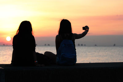 Rear view of women overlooking sea at sunset