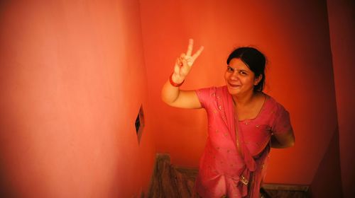 High angle portrait of smiling woman gesturing peace sign at home