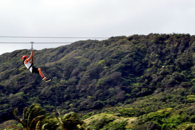 Woman zip lining on mountain against sky