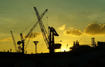 Silhouette cranes against sky at sunset