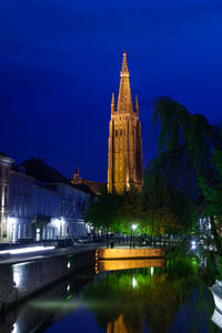 Illuminated building by canal against sky at night