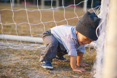 Side view of boy crouching in goal post on soccer field