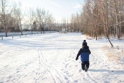 Young boy walking on snow in a park on a sunny day