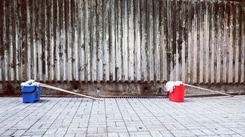 Mops in red and blue buckets on footpath by old wall