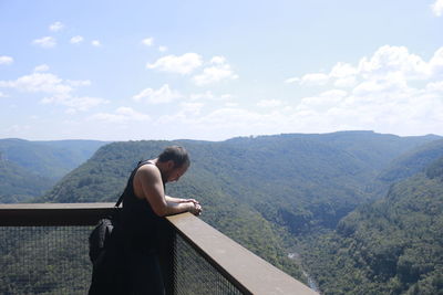 Side view of woman standing on mountain against sky