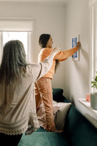 Senior woman assisting granddaughter in arranging painting on wall at home