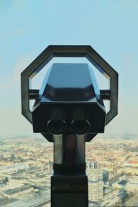 Close-up of binoculars by cityscape against sky