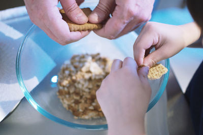 Cropped hands of father and son breaking biscuits in bowl on table