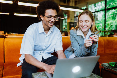 Portrait of smiling friends using laptop at table