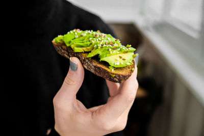 Female hand holding healthy avocado toast. ripe hass avocado, wholegrain bread, sesame flax seeds. 