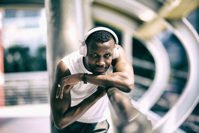 Portrait of man wearing headphones while leaning on railing