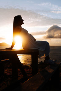 Silhouette man sitting on bench against sky during sunset