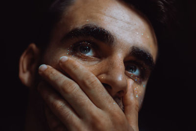 Close-up of man with glitter on face against black background