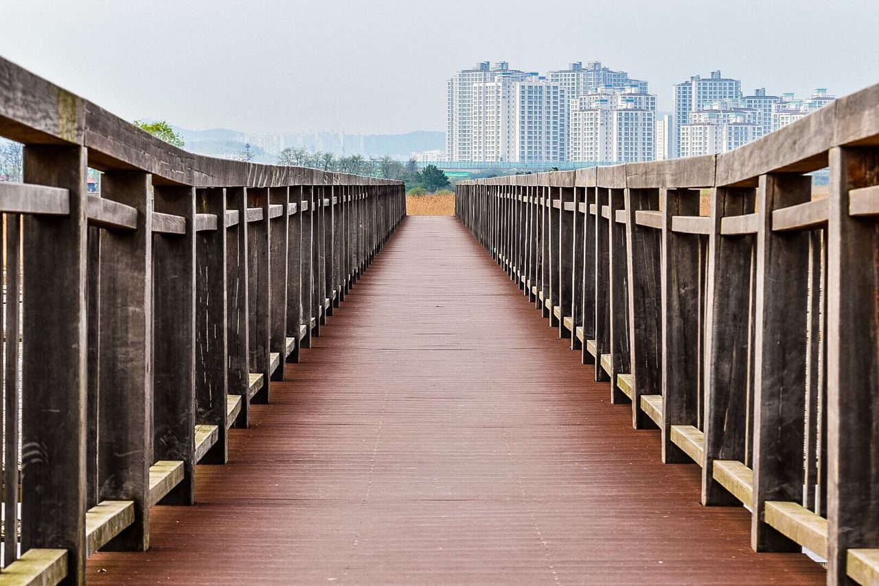 architecture, built structure, building exterior, diminishing perspective, the way forward, railing, clear sky, in a row, footbridge, city, day, wood - material, sky, vanishing point, modern, no people, outdoors, building, repetition, low angle view
