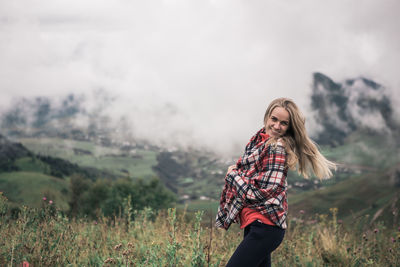 Portrait of smiling young woman standing against landscape 