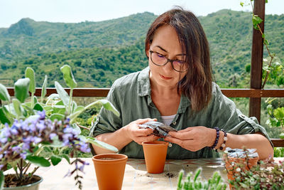 Woman sowing medicinal or aromatic herbs in clay pot on balcony. home planting and food growing.